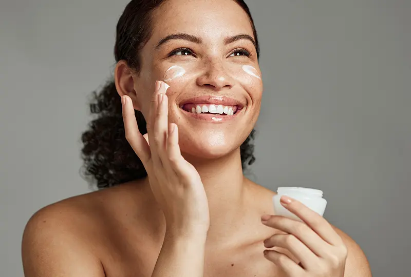 Person smiling and applying face cream.
